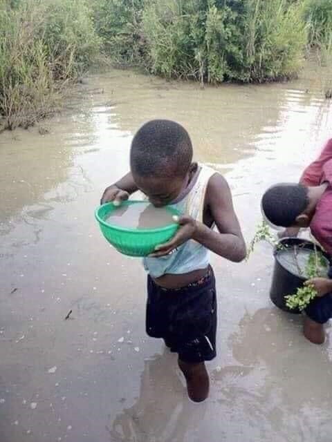 Côte d'Ivoire, les pieds dans l'eau un enfant boit dans une bassine en plastique de l'eau boueuse. 