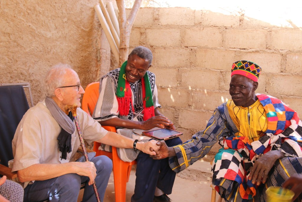 3 vieux monsieurs dont deux se serrent la main. Le président de l'association ADEB au Burkina Faso 