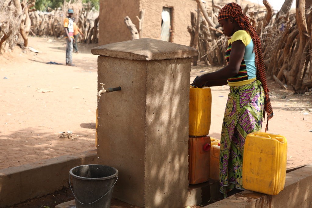 une jeune femme rempli des bidons d'eau à une borne fontaine au Mali