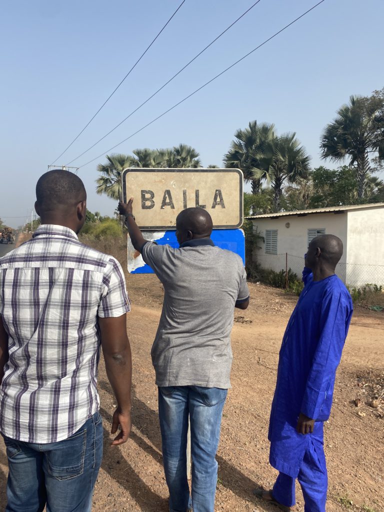 trois hommes debout devant le panneau de la ville de baila au sénégal en jumelage avec houdan dans les yvelines.