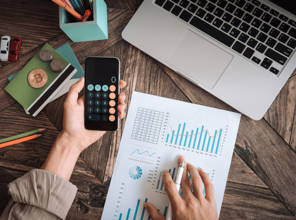 une femme s'occupe du suivi de son projet avec une calculatrice, son ordinateur et des graphiques.